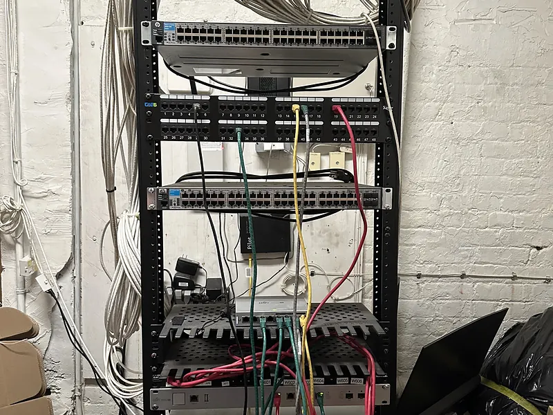 Open network rack with tangled patch cables against a brick wall