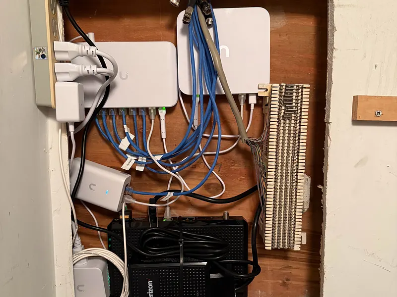 Network gear and blue Ethernet cables inside an in-wall panel in a Chelsea apartment