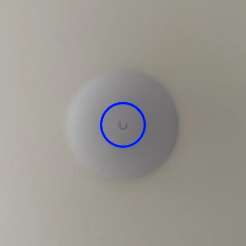 White round UniFi access point on a ceiling with a blue light ring