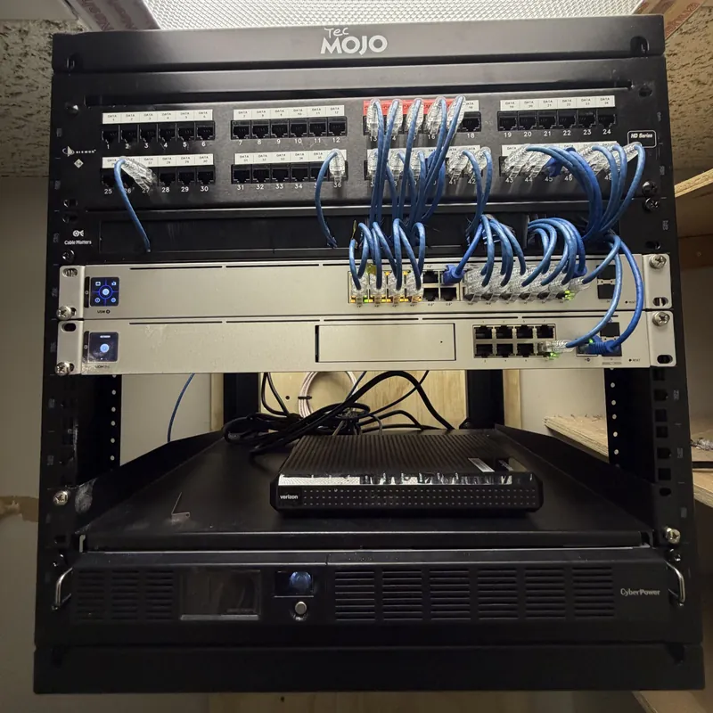 Wall rack with a patch panel, blue patch cables and UniFi network equipment