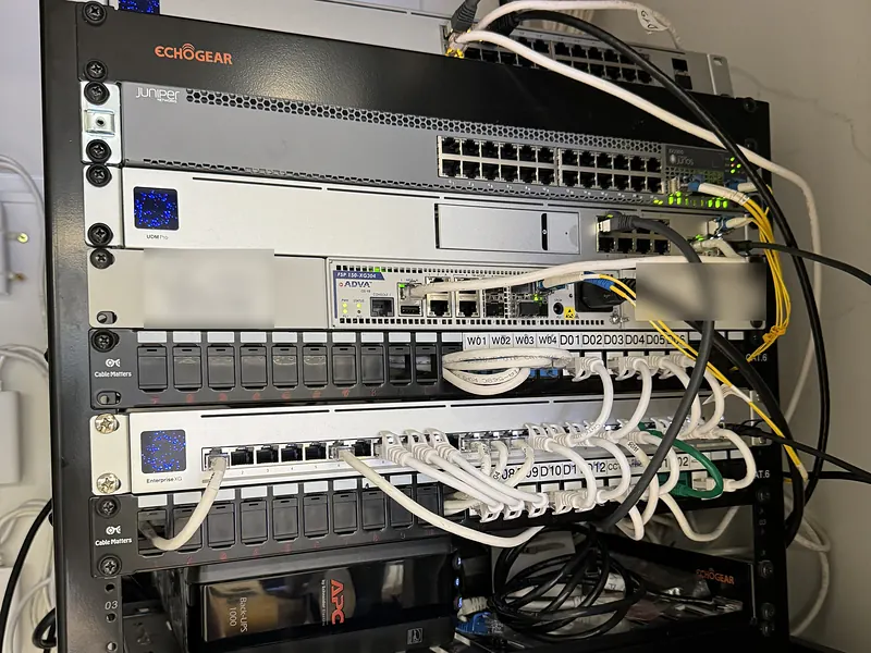 Wall-mounted rack with a UniFi Dream Machine Pro, switches, fiber handoffs and patch panels