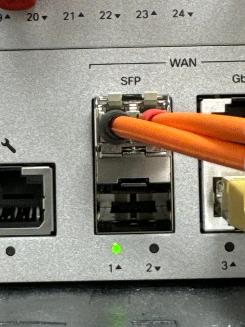Orange fiber cable in the fiber port of a firewall with a green link light