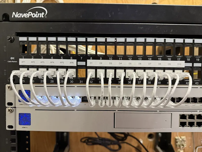 Patch panel labeled AP1 to AP6 and D1 to D10 with short white patch cables into a UniFi switch