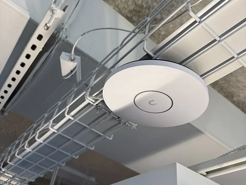 UniFi ceiling access point mounted beside a wire cable tray