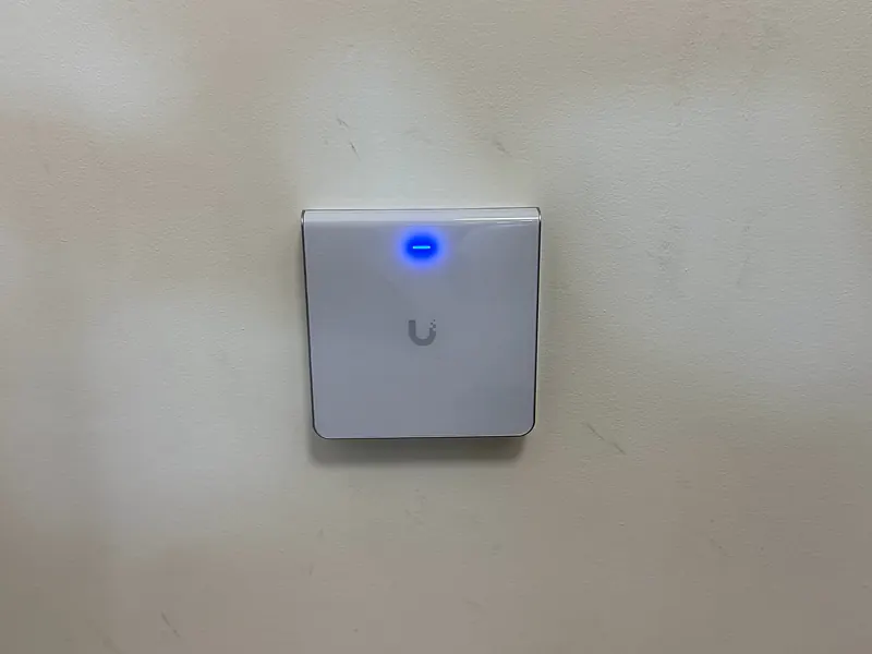 UniFi in-wall access point with a blue status light on an office wall