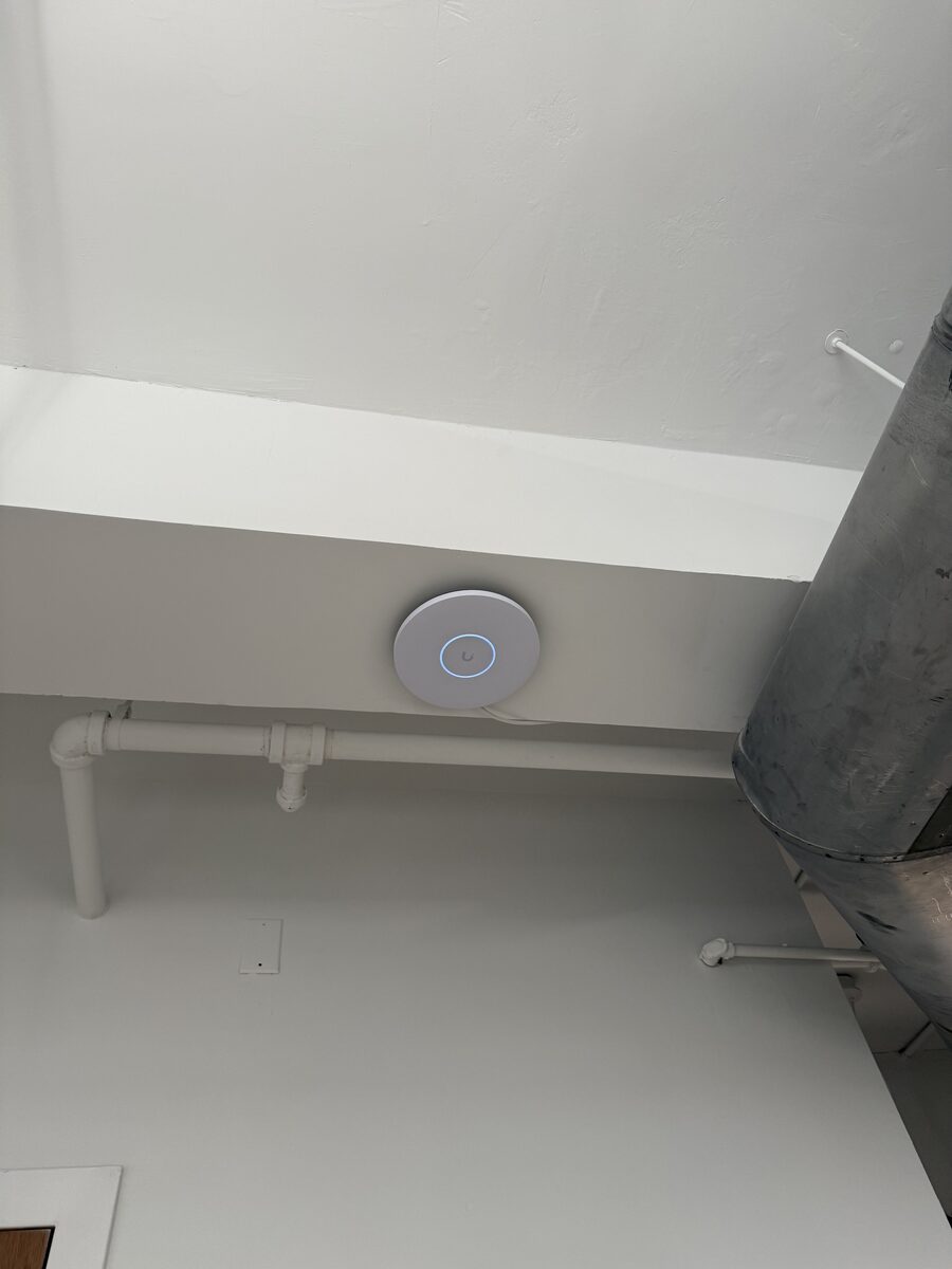UniFi access point mounted on a ceiling beam with blue status ring lit
